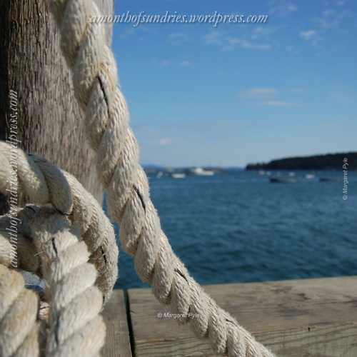 Weathered rope stands ready for service at the pier, with boats in the harbor in the background.